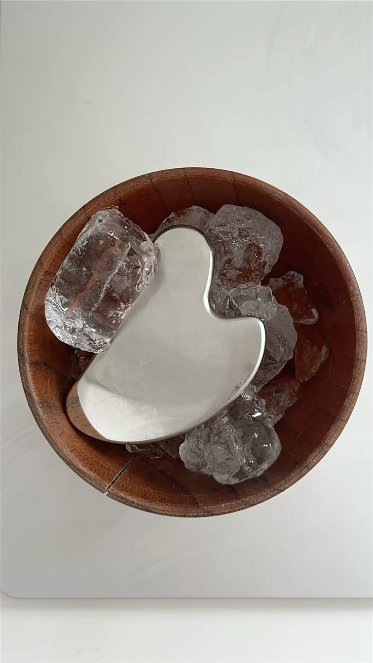 Gua sha en métal poli reposant sur glaçons